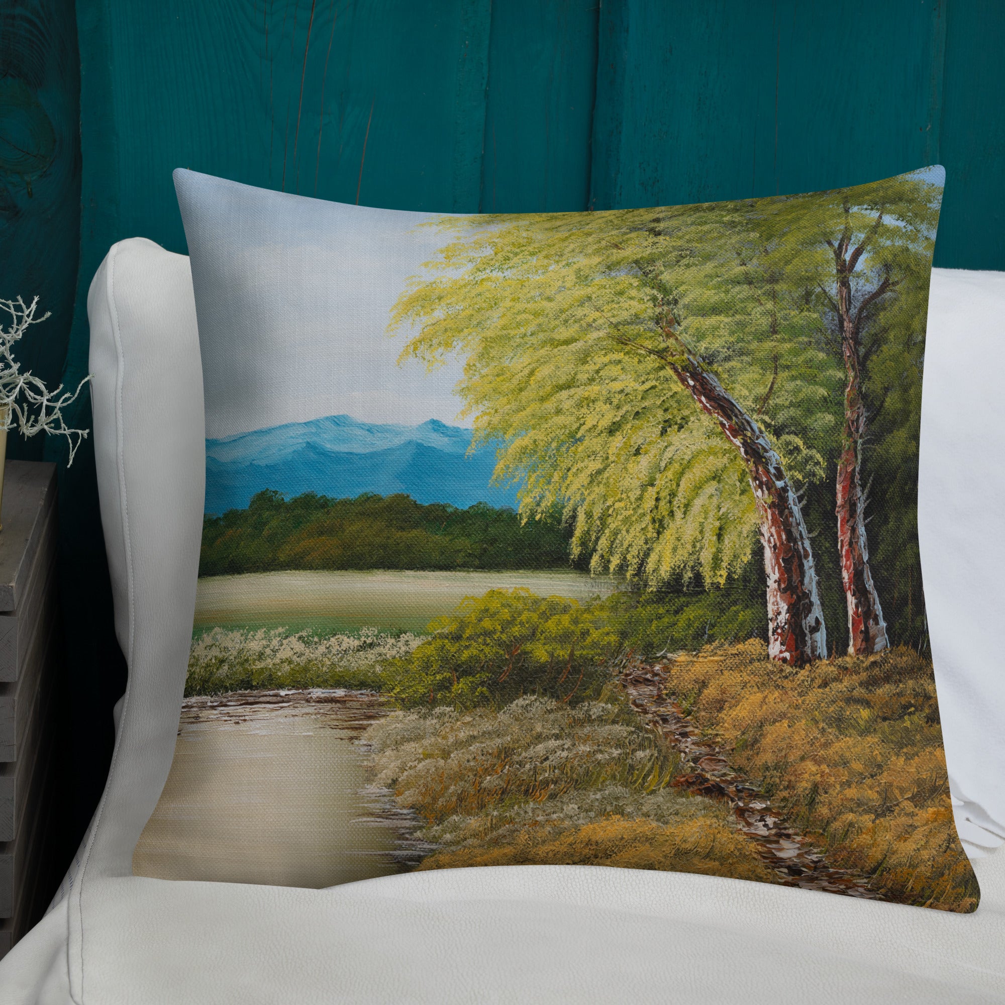 Exclusive and decorative premium designer cushion with an all-over print of a painted landscape with a large glade and a big green tree under a blue sky.