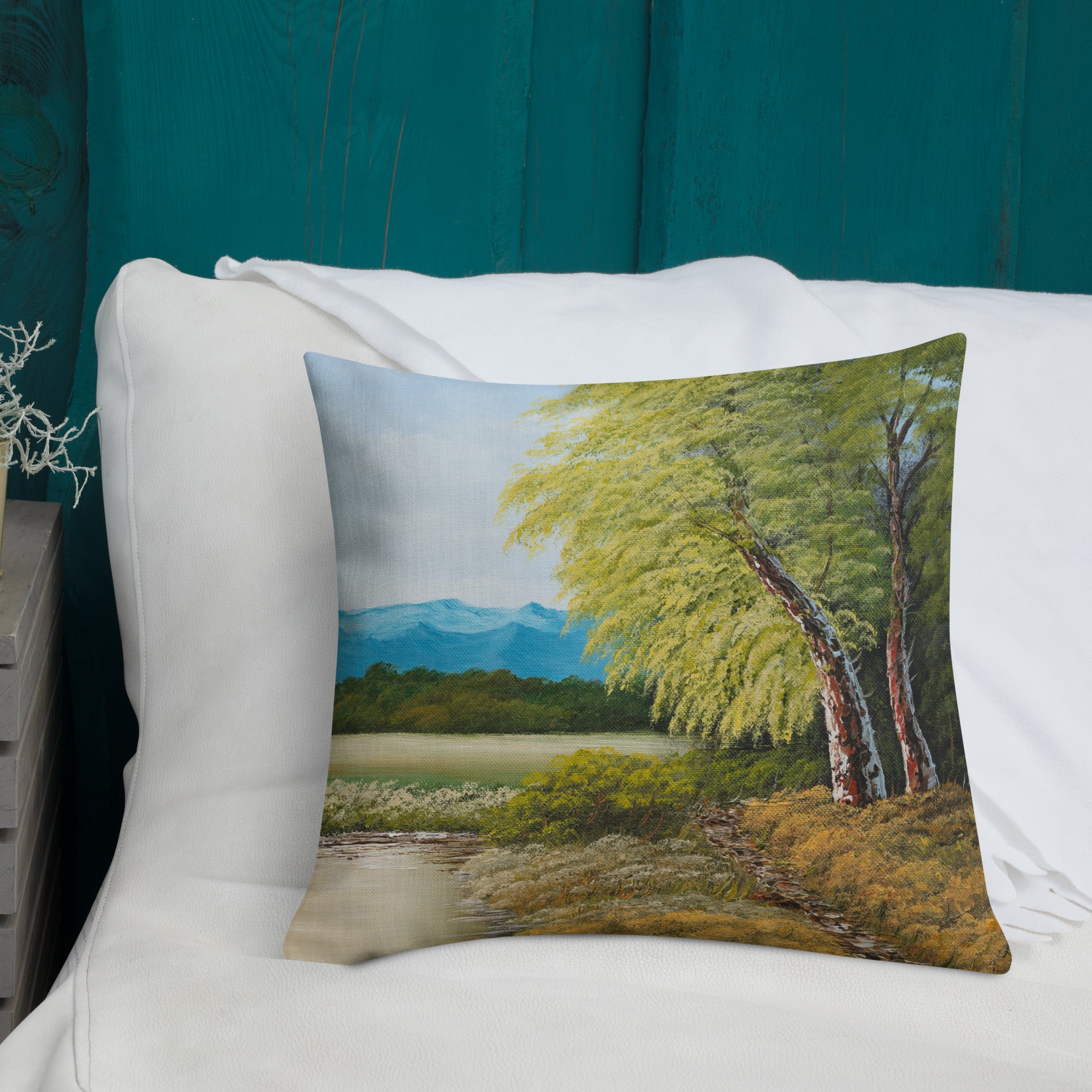 Exclusive and decorative premium designer cushion with an all-over print of a painted landscape with a large glade and a big green tree under a blue sky.