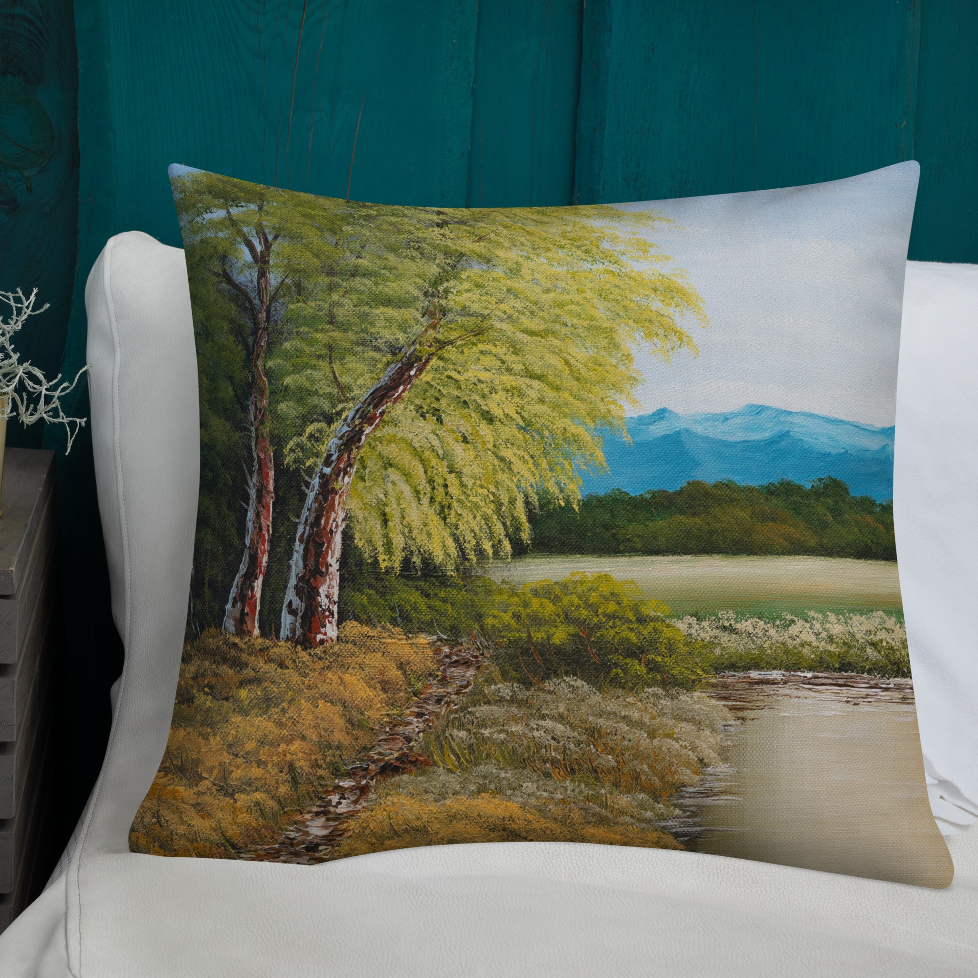Exclusive and decorative premium designer cushion with an all-over print of a painted landscape with a large glade and a big green tree under a blue sky.