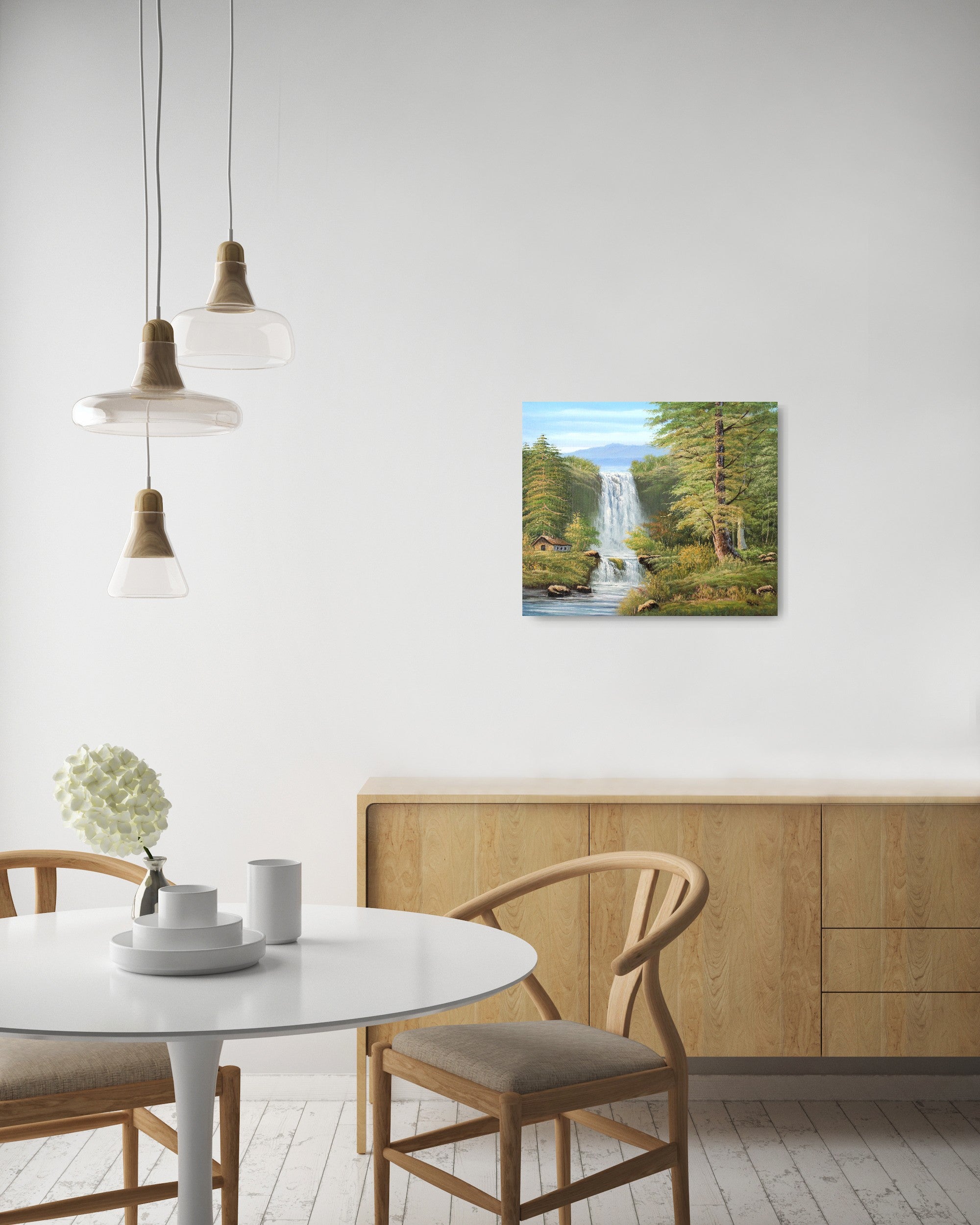 Original artwork by Tobias Nolte titled “Twin Falls”. A hand-painted oil painting (60x50 cm) featuring two cascading waterfalls in a lush forest scene with mountains, tall green trees, and a small wooden cabin by the riverbank, displayed in a modern living room.