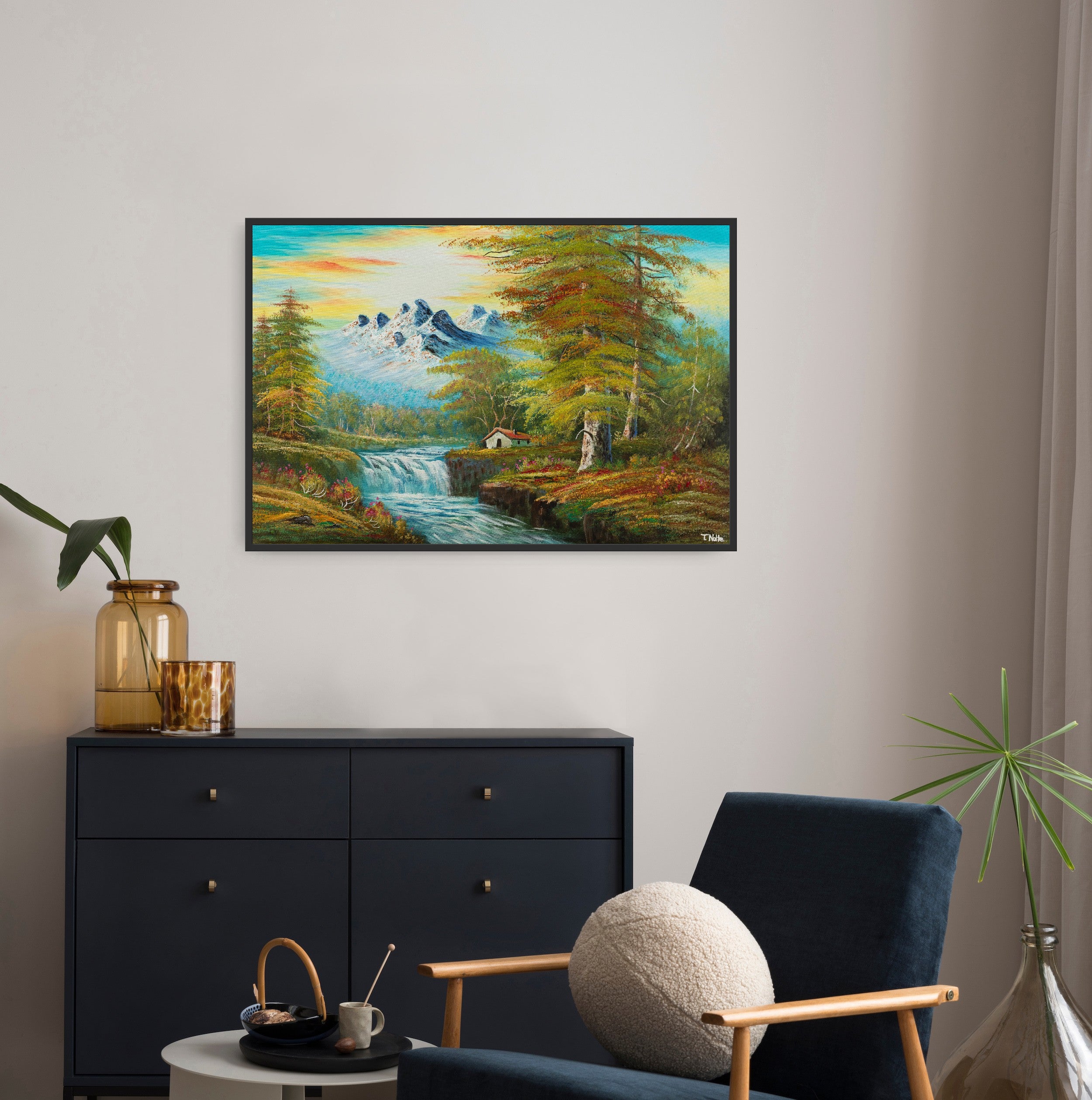 Framed canvas art print of a calm forest landscape with mountains, a cottage next to a river with some waterfalls and lots of trees and bushes, displayed in a modern living room.