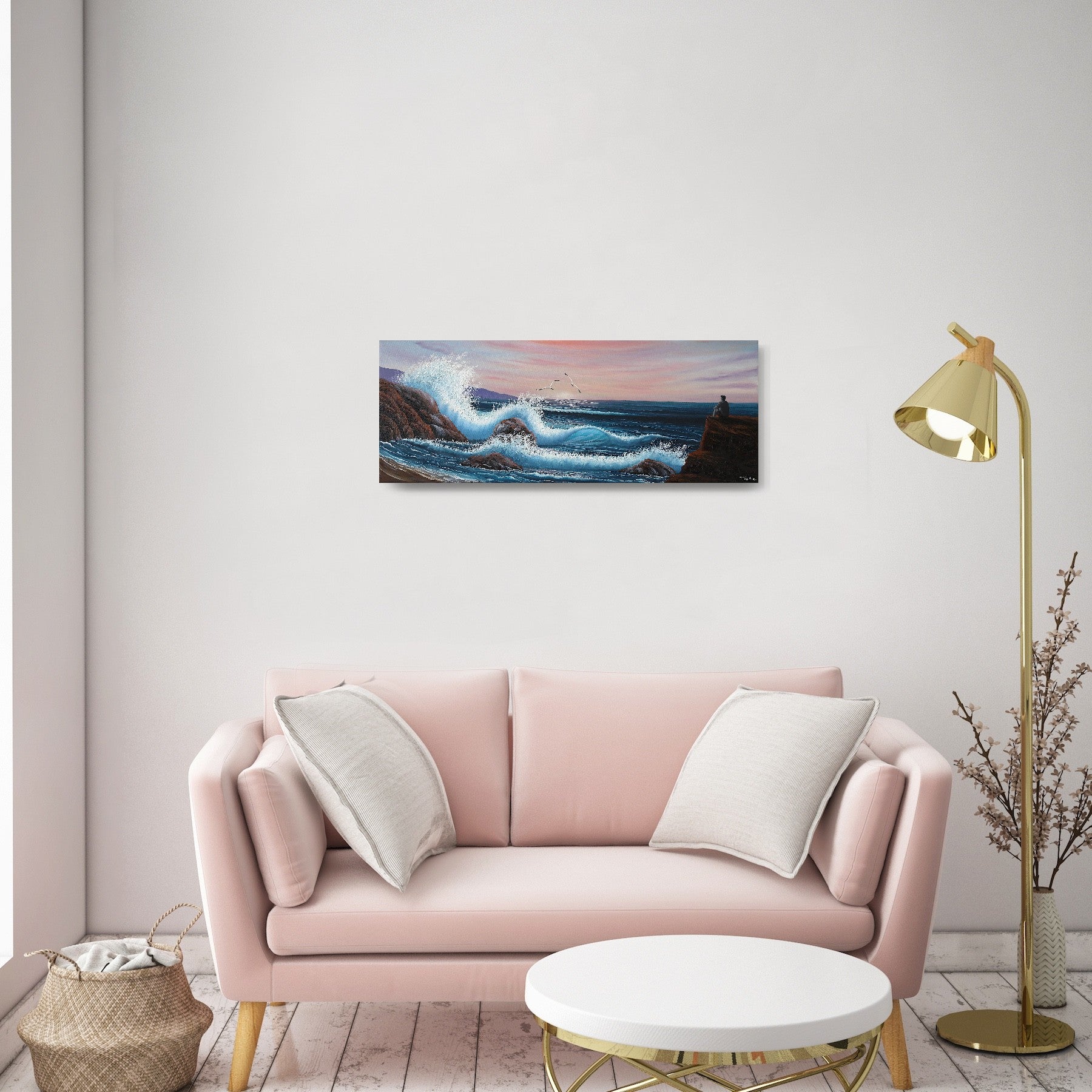 Oil painting on canvas showing a dramatic seascape with large blue waves crashing against rocky cliffs at sunset. Pink and purple clouds fill the sky. A grey person sits on a rock, gazing out at the ocean. The painting is shown in a modern living room.