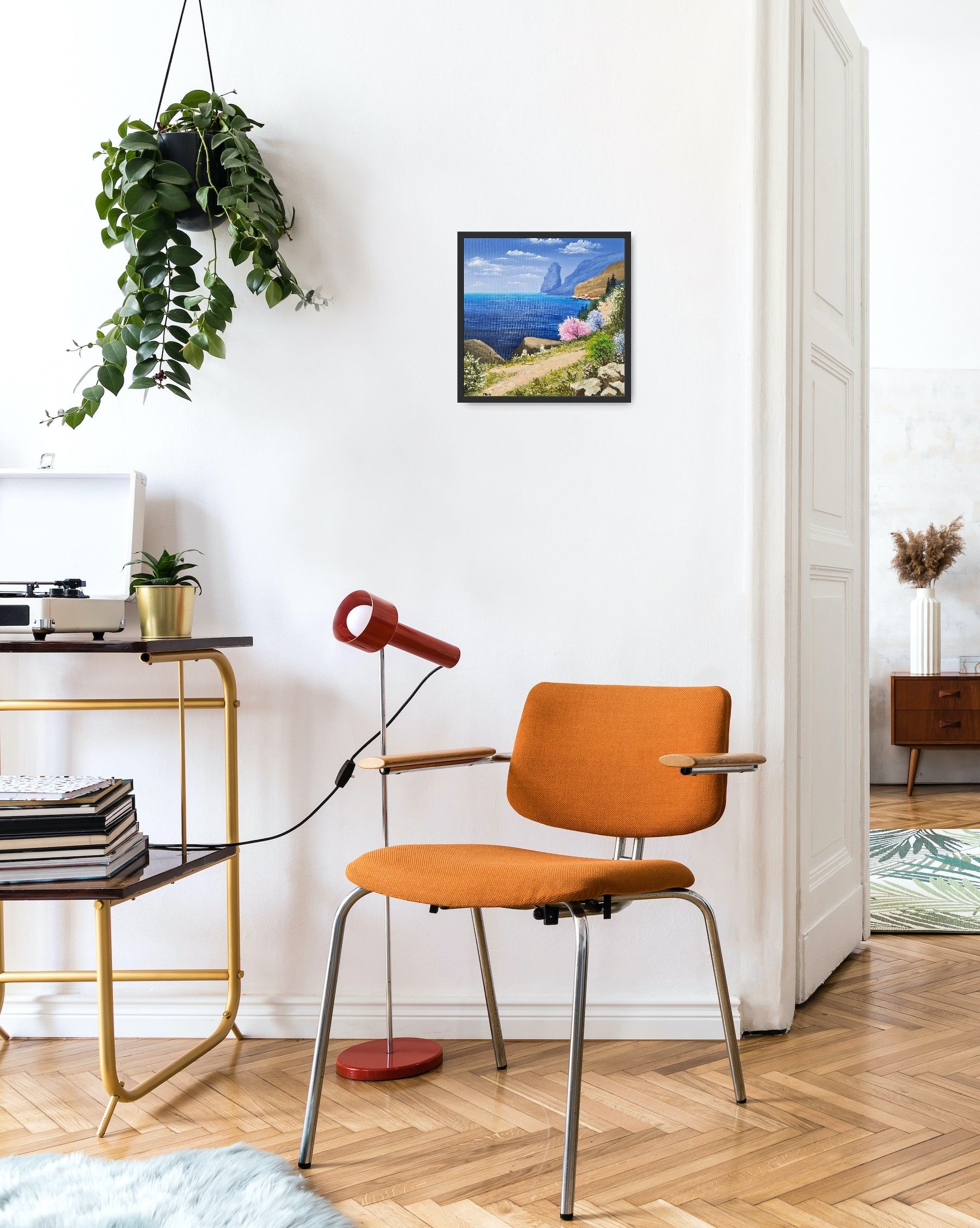 Original artwork by Tobias Nolte titled “Sea View”. A framed, hand-painted oil painting (30x30 cm) featuring a blue sea panorama along a hiking trail, next to colorful trees and rocks, displayed in a modern living room.