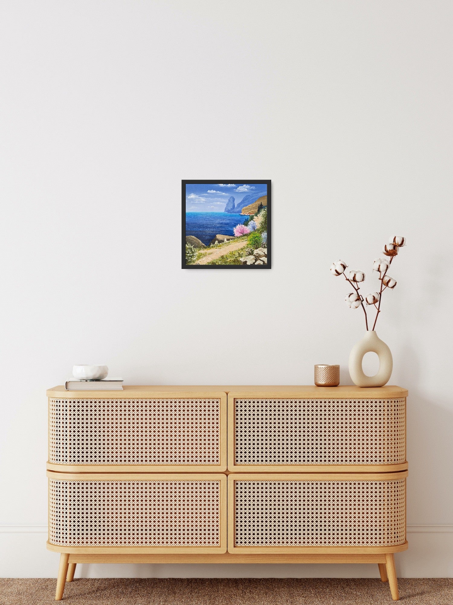 Original artwork by Tobias Nolte titled “Sea View”. A framed, hand-painted oil painting (30x30 cm) featuring a blue sea panorama along a hiking trail, next to colorful trees and rocks, displayed in a modern interior setting.
