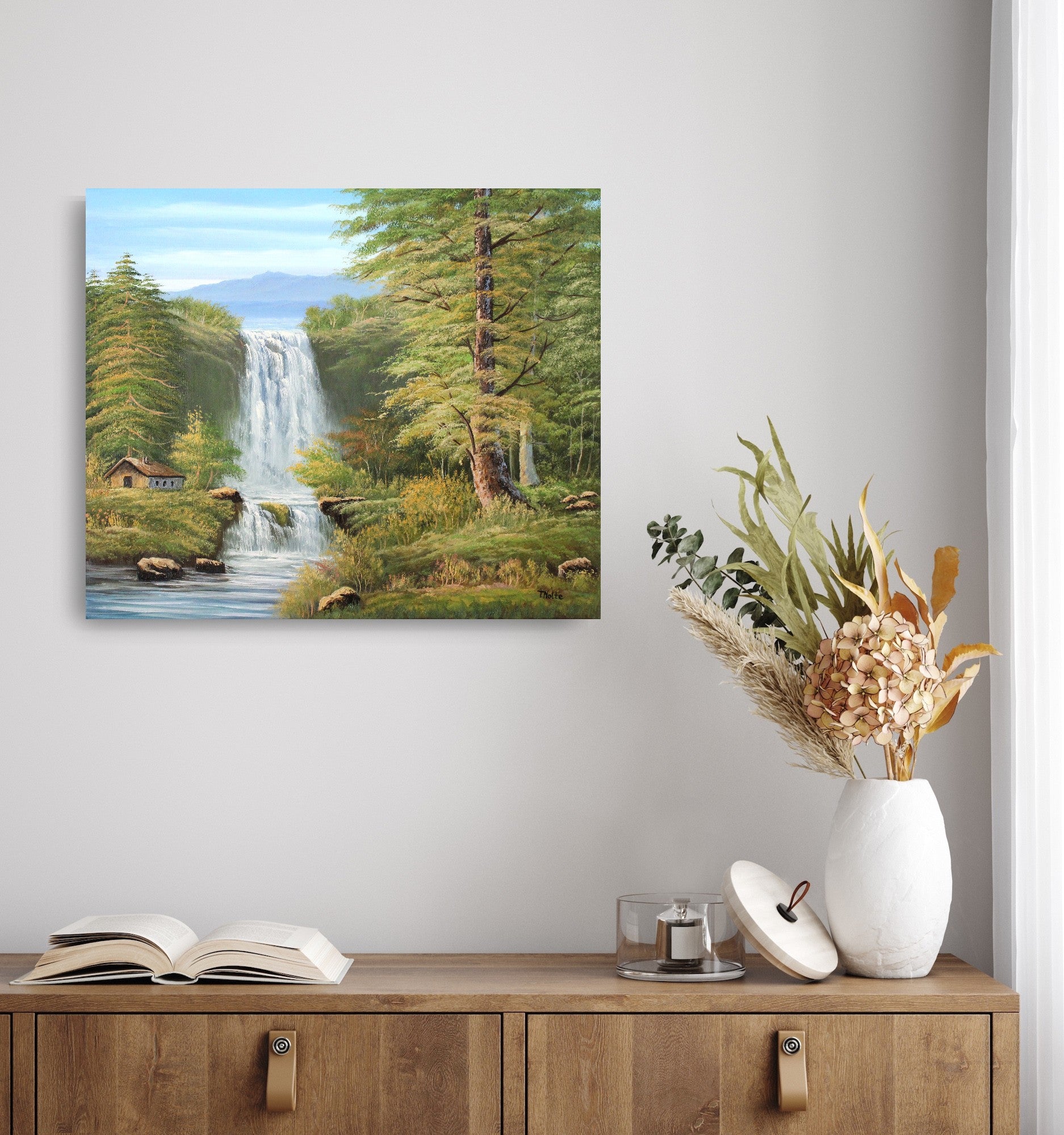 Original artwork by Tobias Nolte titled “Twin Falls”. A hand-painted oil painting (60x50 cm) featuring two cascading waterfalls in a lush forest scene with mountains, tall green trees, and a small wooden cabin by the riverbank, displayed on the wall.